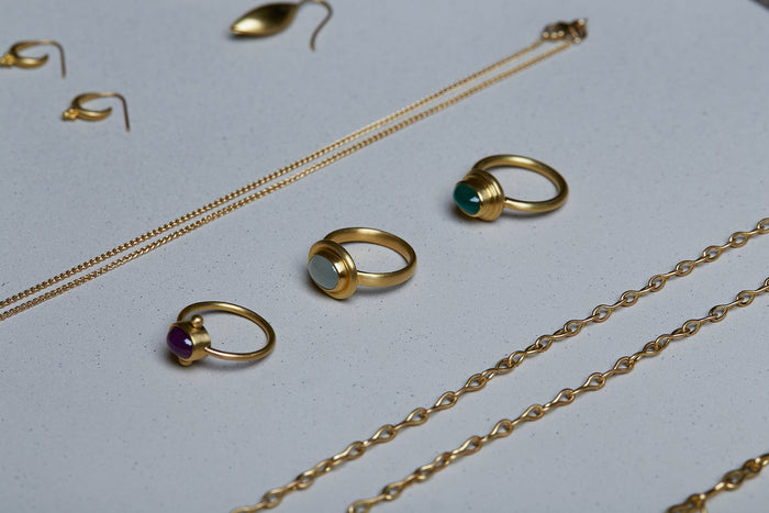 Collection of three 22k gold rings handmade by Alexis Menten in an ancient style displayed next to other chains and earrings