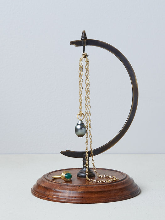 A necklace handmade by Alexis Menten with a gray South Sea pearl pendant on an ancient style chain hanging from a metal hook