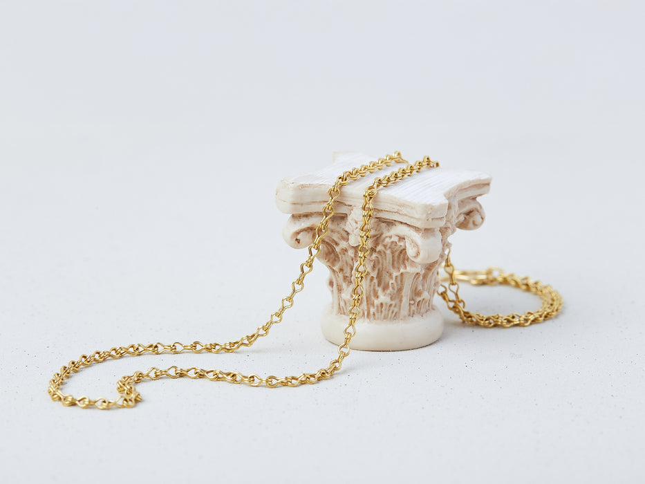 Apeiron Chain by Alexis Menten with intricate 22k gold links handmade in an ancient style displayed on a small column capital