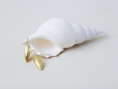 Cylichna Earrings by Alexis Menten with 22k gold cylinders with tapered ends handmade in an ancient style shown on a seashell