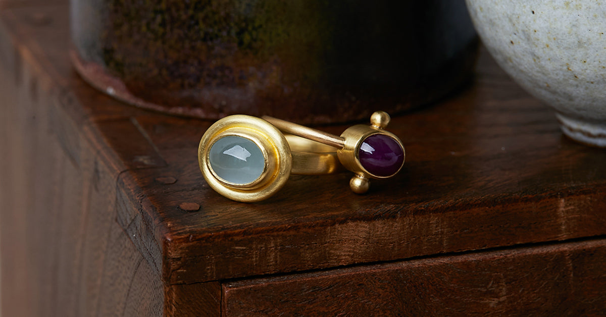 Two ancient style rings handmade by Alexis Menten in 22k gold displayed on an antique wooden box next to two ceramic vessels