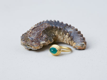 Hellenistic Ring by Alexis Menten handmade in an ancient style with 22k gold and an emerald displayed next to a fossil