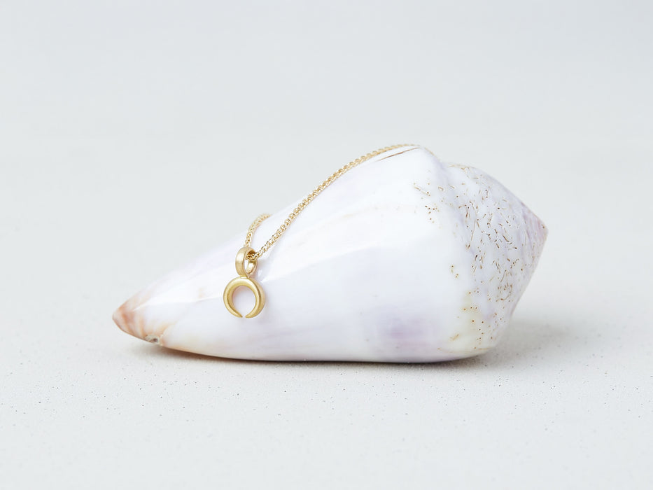 Lunula Necklace by Alexis Menten with a 22k gold crescent shaped pendant handmade in an ancient style shown on a seashell