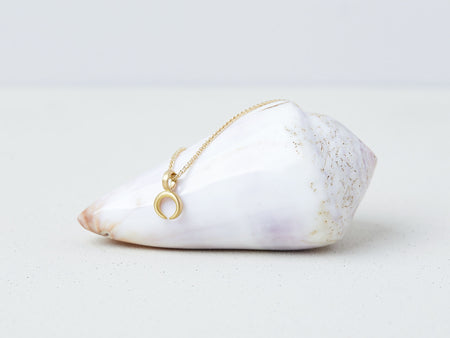 Lunula Necklace by Alexis Menten with a 22k gold crescent shaped pendant handmade in an ancient style shown on a seashell