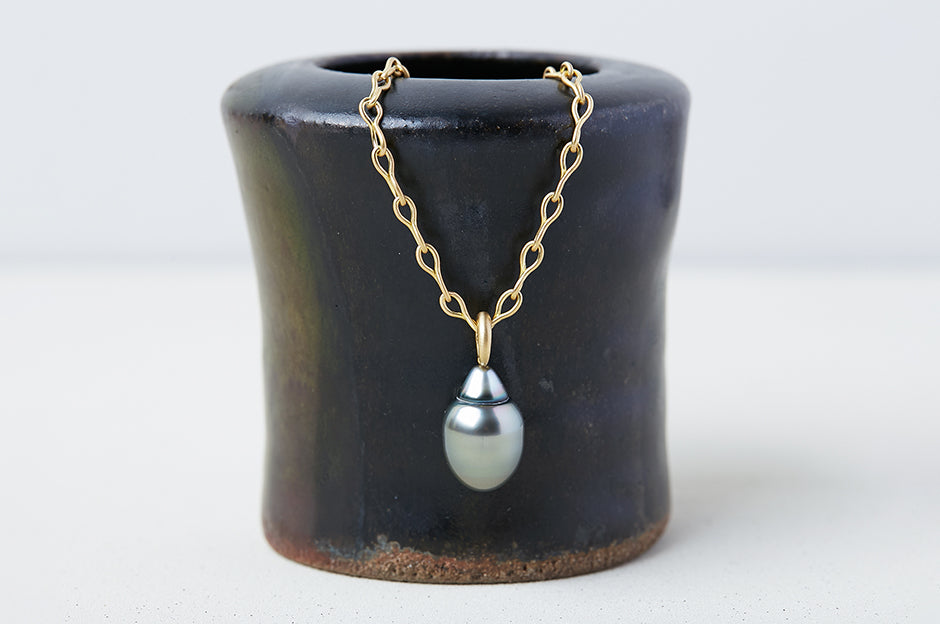 A necklace handmade by Alexis Menten with an ancient style 20k gold chain and gray South Sea pearl pendant on a small vase