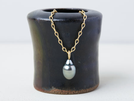 Nuru Chain handmade by Alexis Menten with an ancient style 20k gold chain and gray South Sea pearl pendant on a small vase