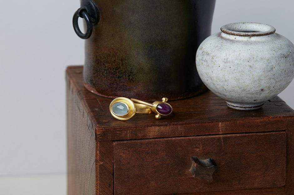 Two ancient style rings handmade by Alexis Menten in 22k gold displayed on an antique wooden box next to two ceramic vessels