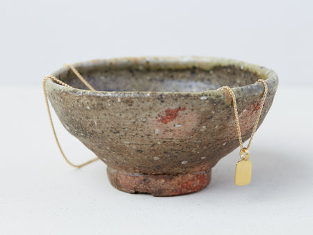 Stele Necklace by Alexis Menten with a rectangular 22k gold pendant handmade in an ancient style displayed on a ceramic bowl